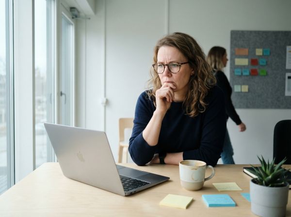 Nainen työskentelee kannettavalla tietokoneella valoisassa suomalaisessa toimistossa koivupuisen työpöydän ääressä